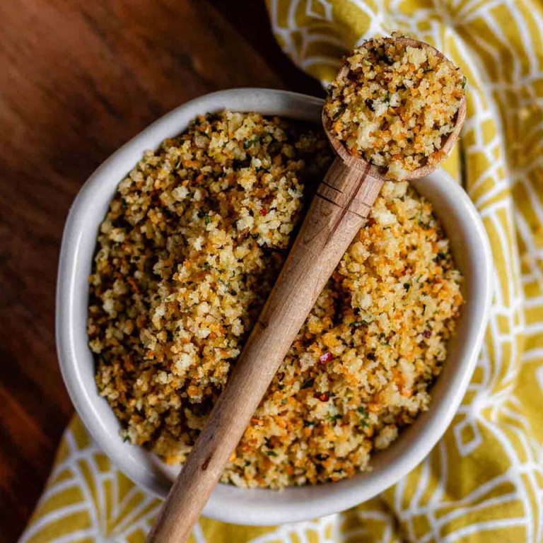 Browned panko breadcrumbs in a bowl with a spoon of breadcrumbs resting over the top.