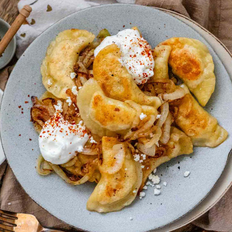 Pierogis on a plate with sour cream, feta cheese, and fried onions.