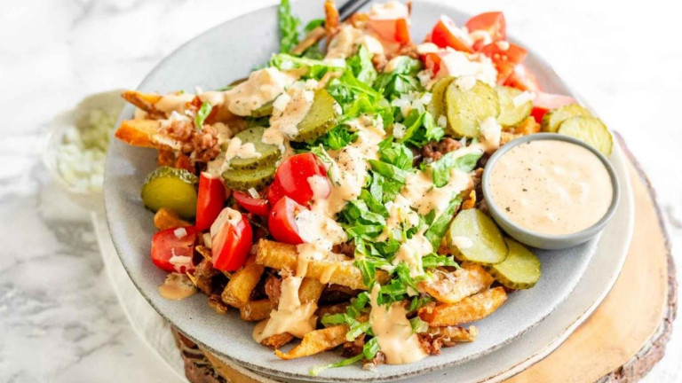 Fries topped with tomatoes, pickles, lettuce, and sauce.