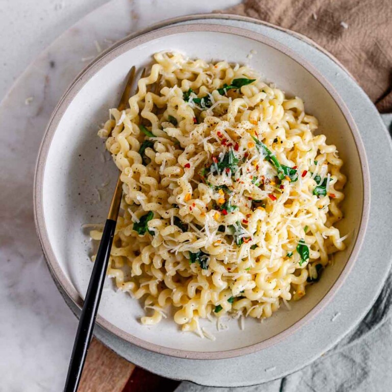 Long curly pasta in a bowl topped with cheese and red pepper flakes.