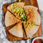 A quesadilla on a wooden board, cut into 6 slices and topped with lettuce.
