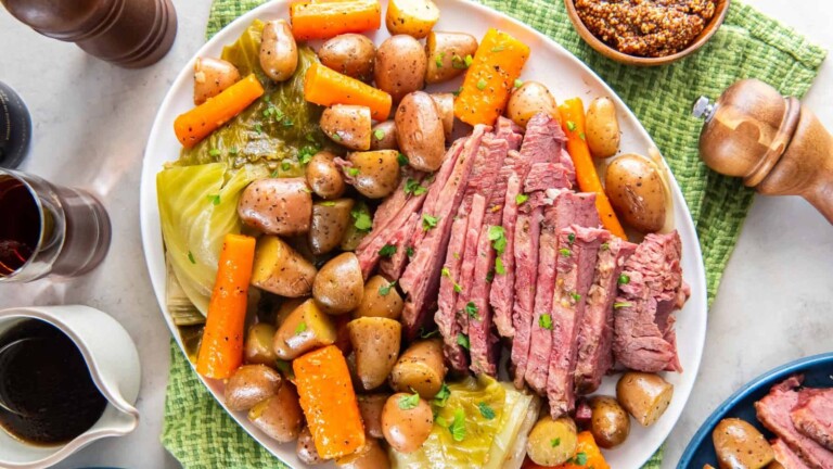 A white plate of sliced corned beef, carrots, potatoes, and cabbage, sprinkled with parsley.