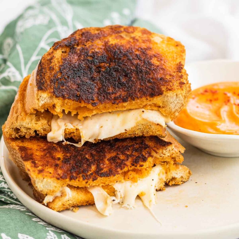 A halved, stacked grilled cheese sandwich on a plate with a bowl of dip.
