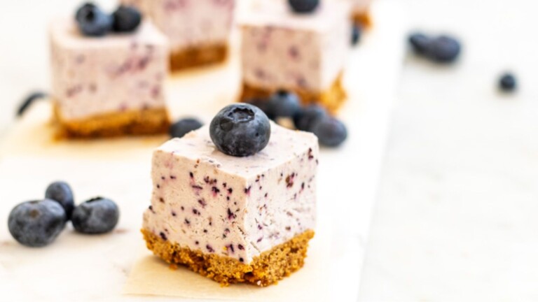 A blueberry cheesecake square topped with a fresh blueberry.