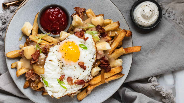 Fries topped with cheese curds, gravy, bacon, fried onions, a fried egg, and green onion.