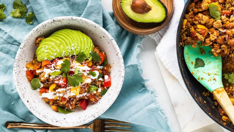A skillet and bowl with ground turkey and vegetables in it, with avocado slices on top and a halved avocado in a bowl.
