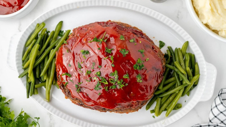 Meatloaf topped with sauce on a platter with green beans.