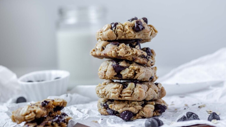 Oatmeal chocolate chip cookies stacked on parchment paper with chocolate chips scattered around.