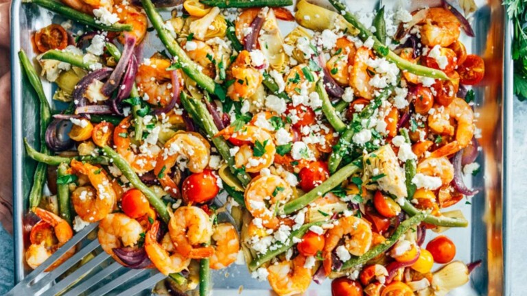 A sheet pan with shrimp, green beans, tomatoes, and cheese.