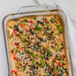 A baked rice casserole in a clear casserole dish, topped with hot sauce, nori, and green onions.