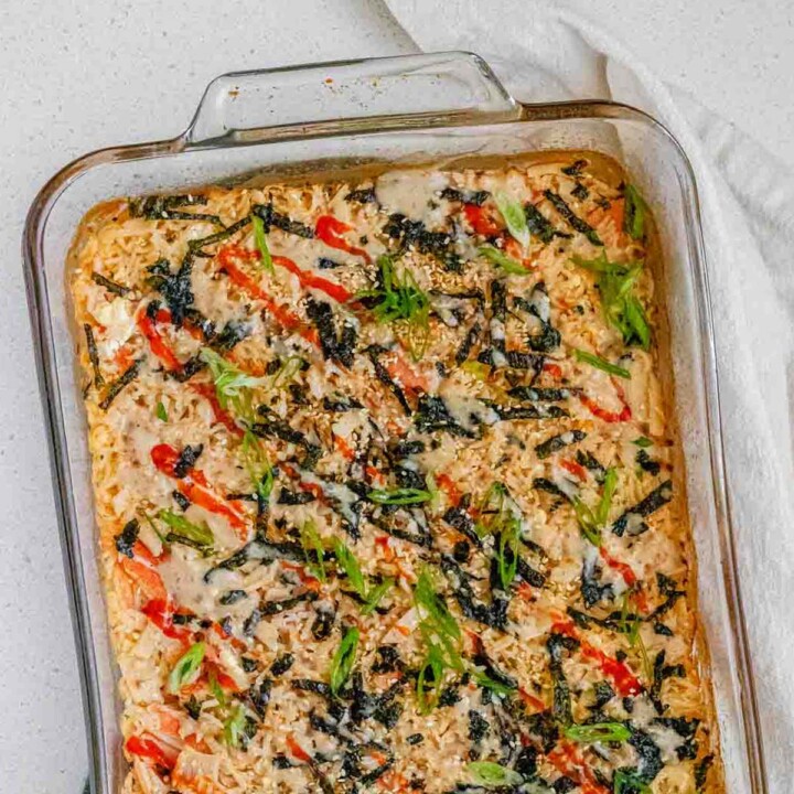 A baked rice casserole in a clear casserole dish, topped with hot sauce, nori, and green onions.