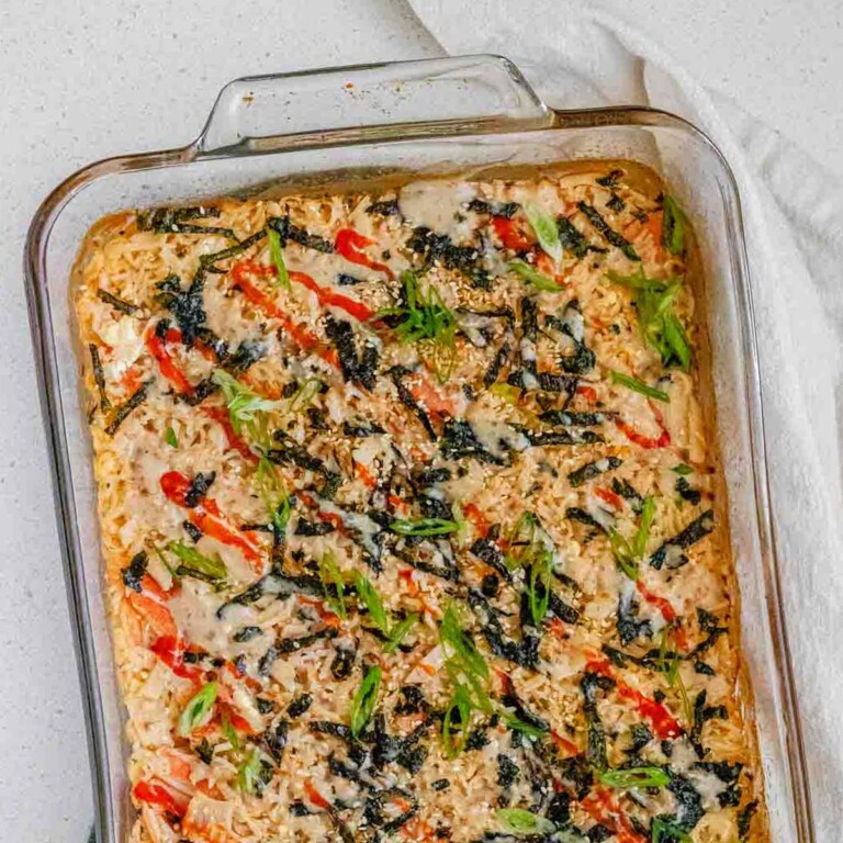 A baked rice casserole in a clear casserole dish, topped with hot sauce, nori, and green onions.