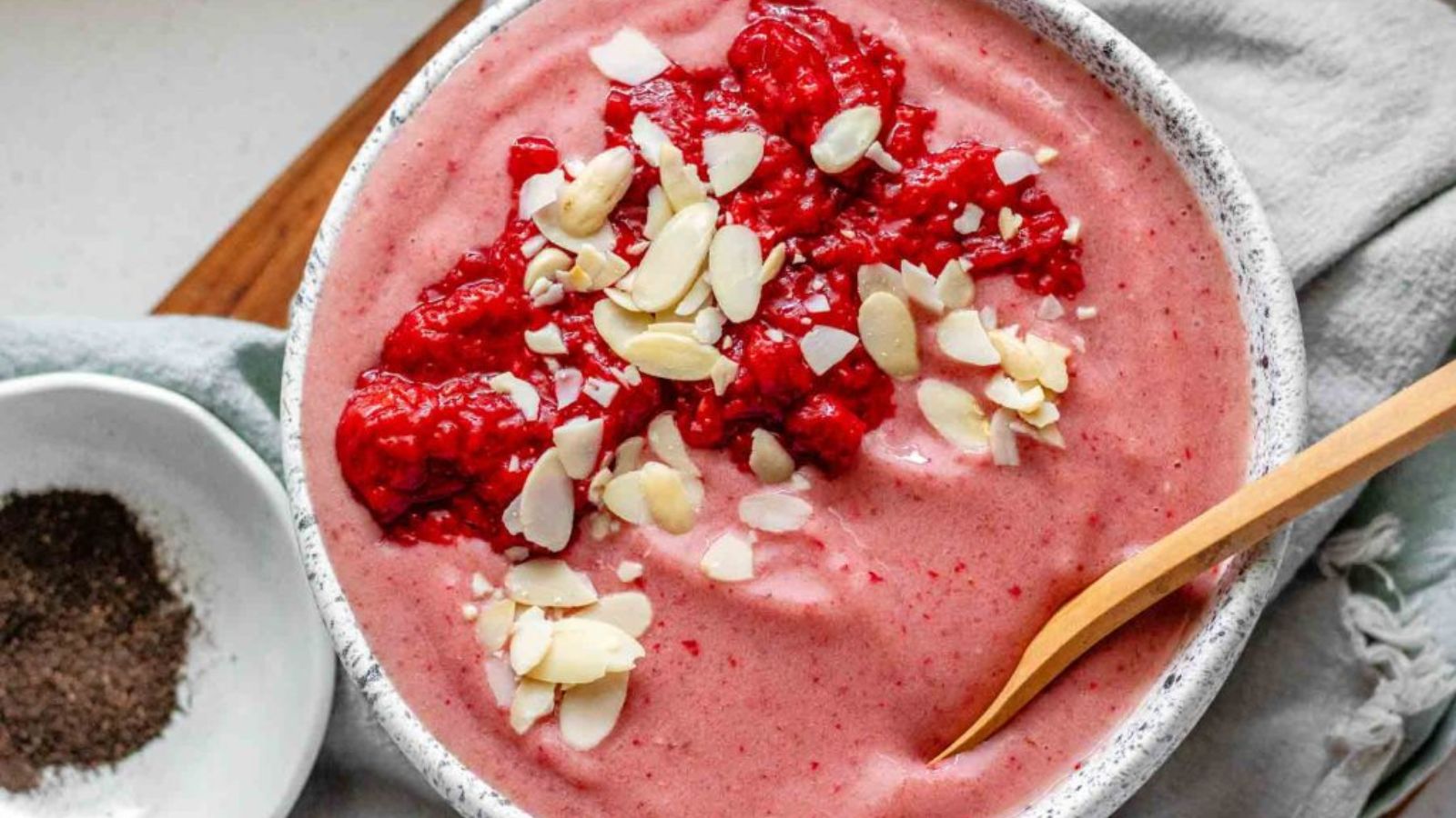 Pink smoothie bowl topped with sliced almonds and strawberry puree.