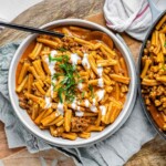 Saucy pasta in a bowl topped with a drizzle of white sauce and sliced green onions.