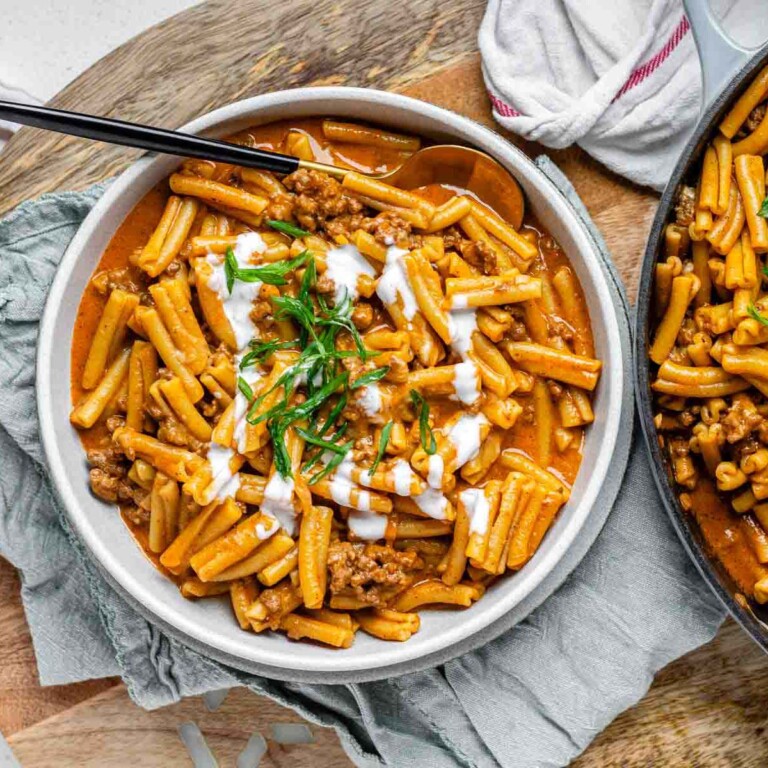 Saucy pasta in a bowl topped with a drizzle of white sauce and sliced green onions.