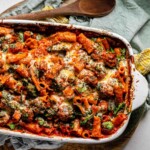 A casserole dish with cooked pasta, spinach, and sausage topped with melted cheese.