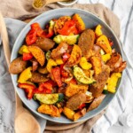 Cooked sweet potato, bell pepper, zucchini, and sausage slices in a bowl.