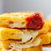 Round yellow corn dough appetizers are stacked on a platter, cut in half, one has red sauce on the end.