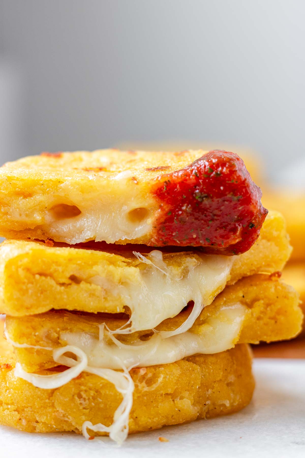 Round yellow corn dough appetizers are stacked on a platter, cut in half, one has red sauce on the end.
