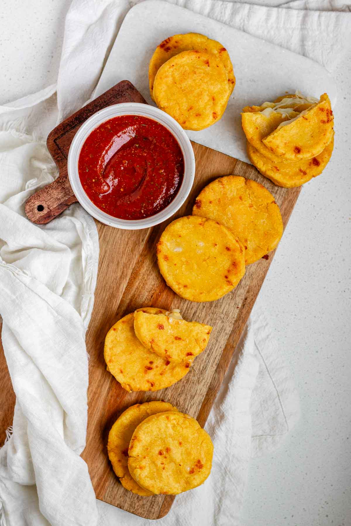 Round yellow corn dough appetizers on a platter beside a bowl of red sauce.