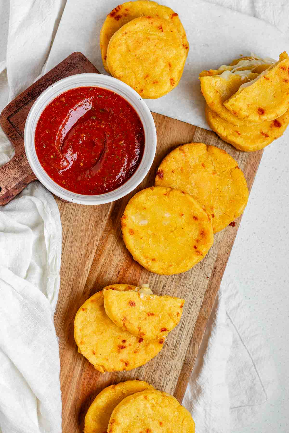 Round yellow corn dough appetizers on a platter beside a bowl of red sauce.