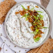 A bowl of white chunky dip with caramelized onion and sliced green onions.