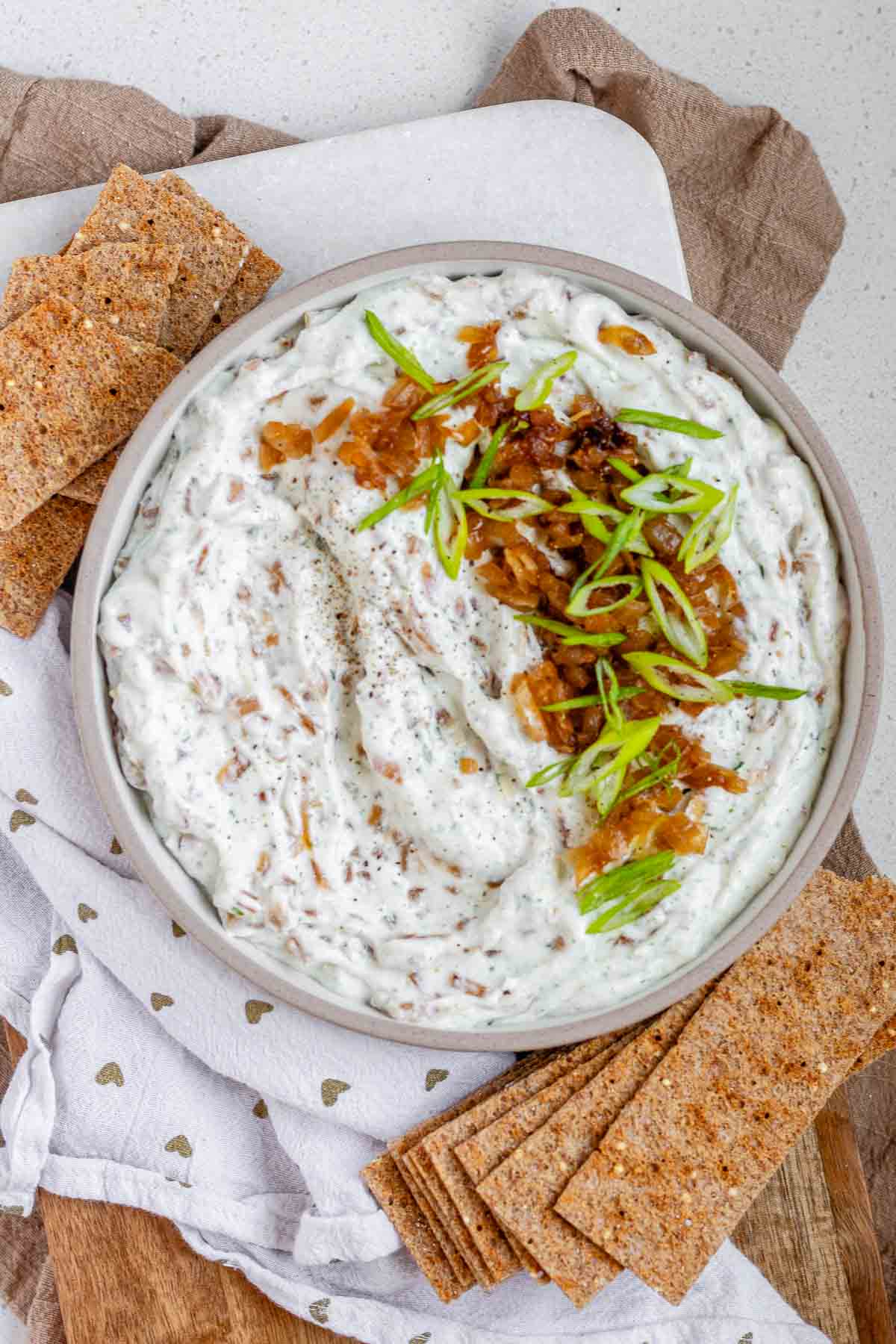 A bowl of white chunky dip with caramelized onion and sliced green onions.
