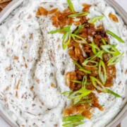 A bowl of white chunky dip with caramelized onion and sliced green onions.