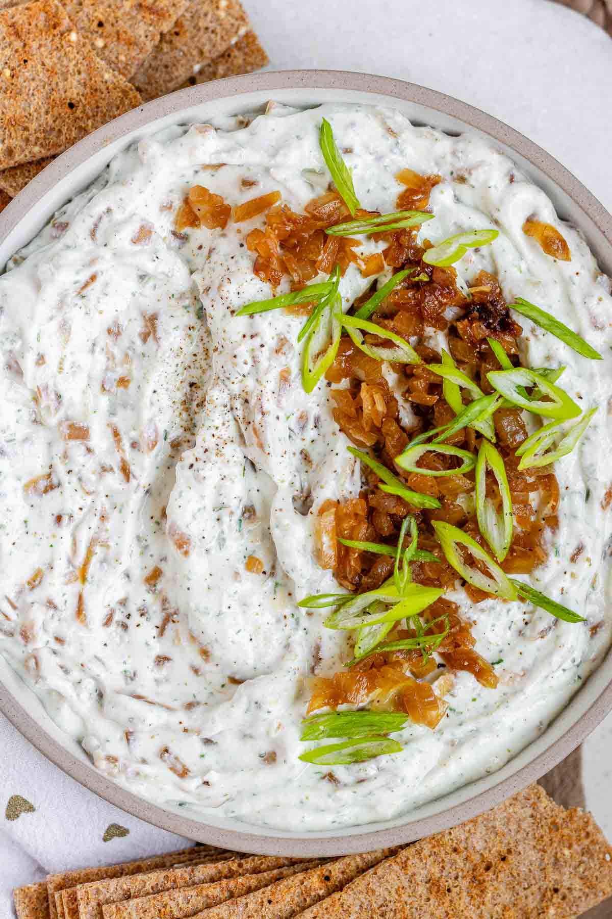 A bowl of white chunky dip with caramelized onion and sliced green onions.