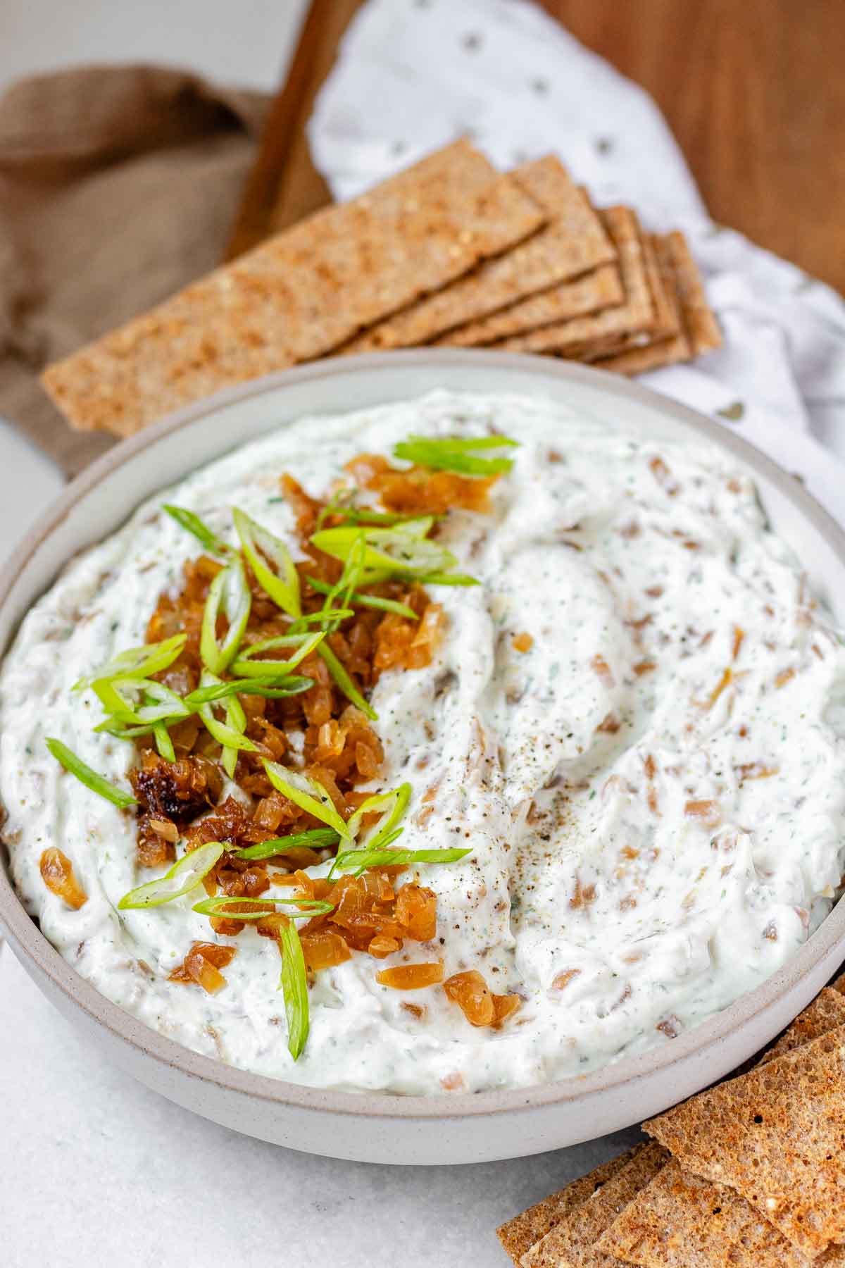 A bowl of white chunky dip with caramelized onion and sliced green onions.