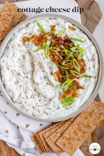 A bowl of white chunky dip with caramelized onion and sliced green onions with the text cottage cheese dip.