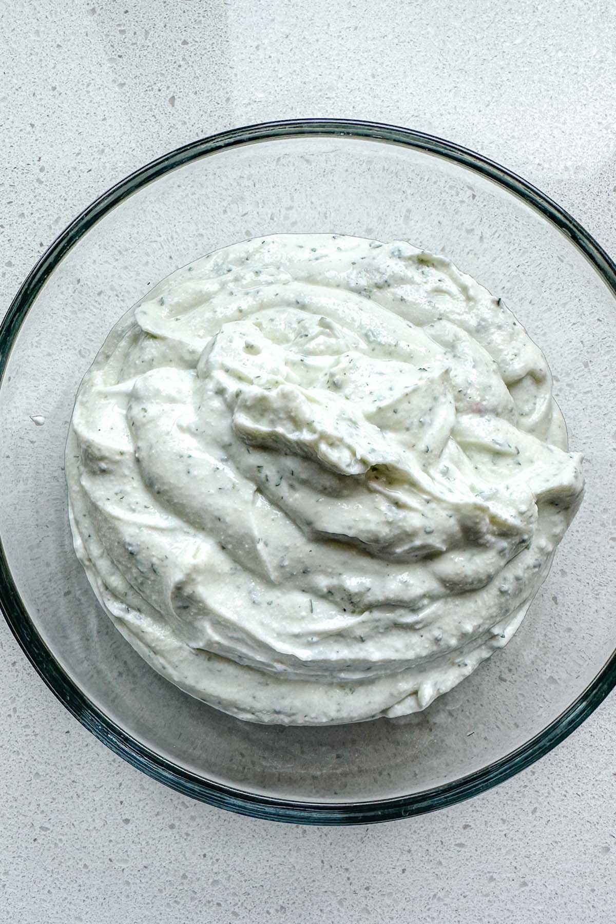 Yogurt with dried herbs blended into it in a bowl.