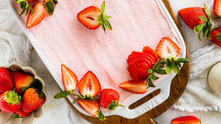 A baking dish with a dessert covered in pink whipped topping and fresh sliced strawberries.