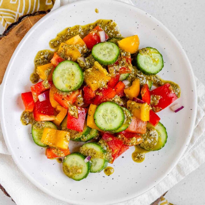 Sliced cucumbers and bell peppers on a plate with pesto dressing on top.