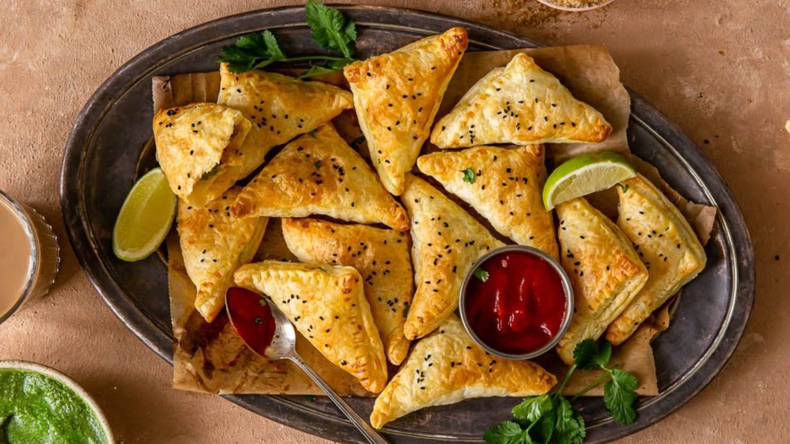 Triangle baked pastries on a serving dish with red dip.
