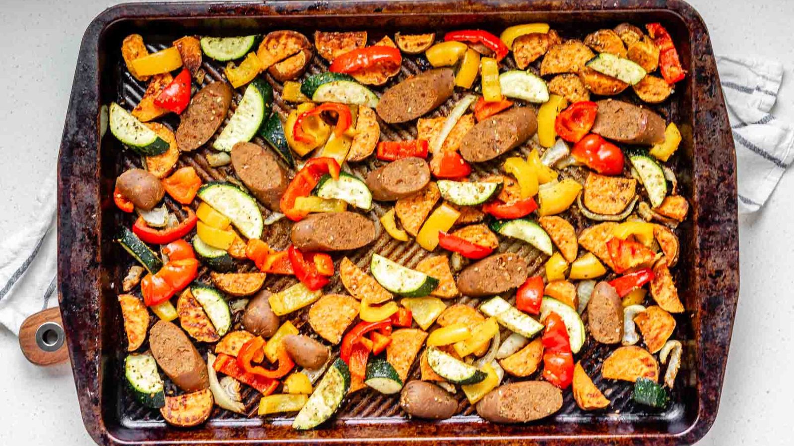 Cooked sweet potato, bell pepper, zucchini, and sausage slices on a baking sheet.