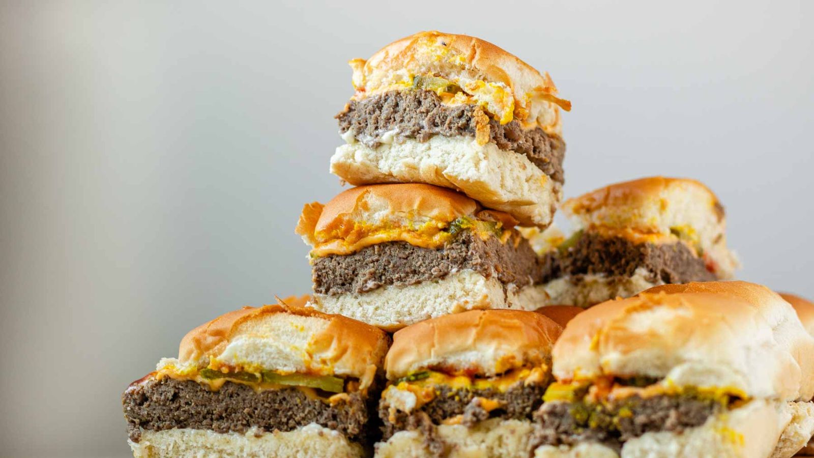 Mini burgers stacked in a pile with a bite out of one.