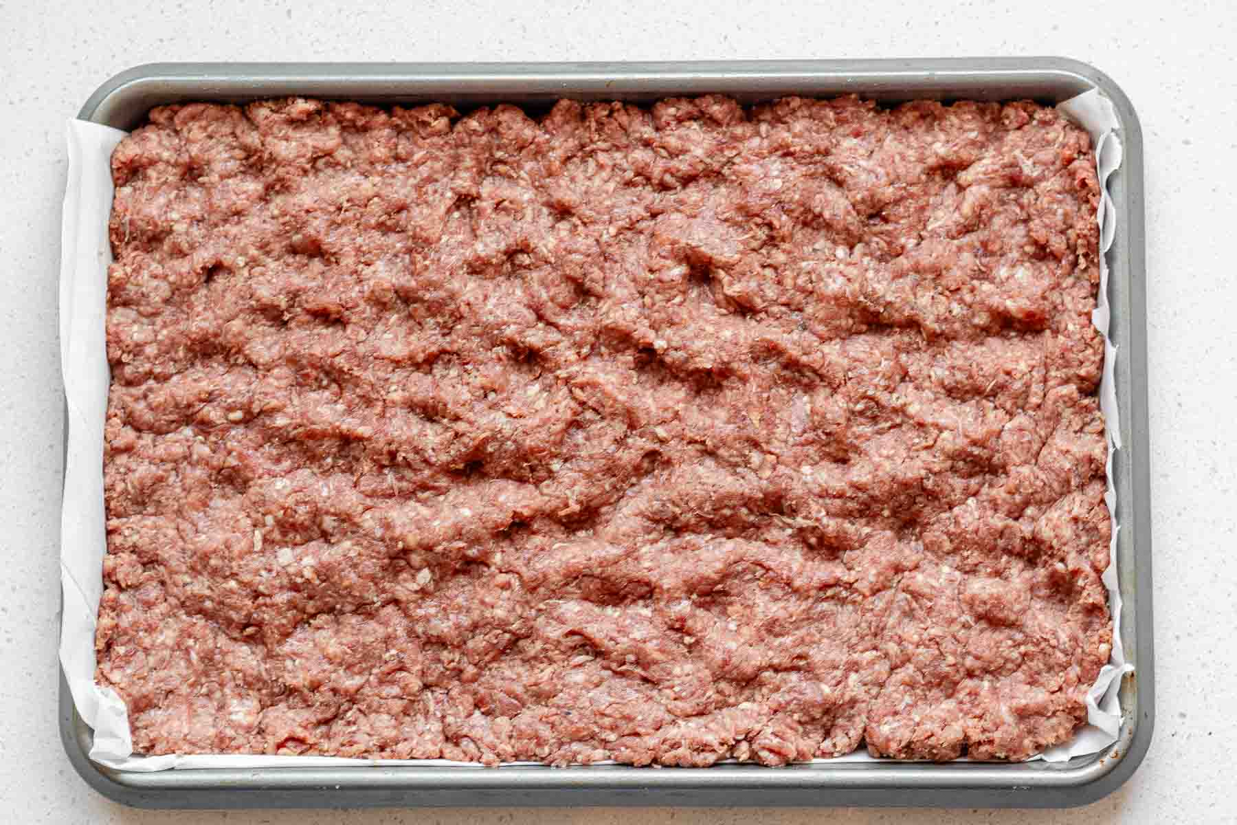 Ground beef spread out on a sheet pan.