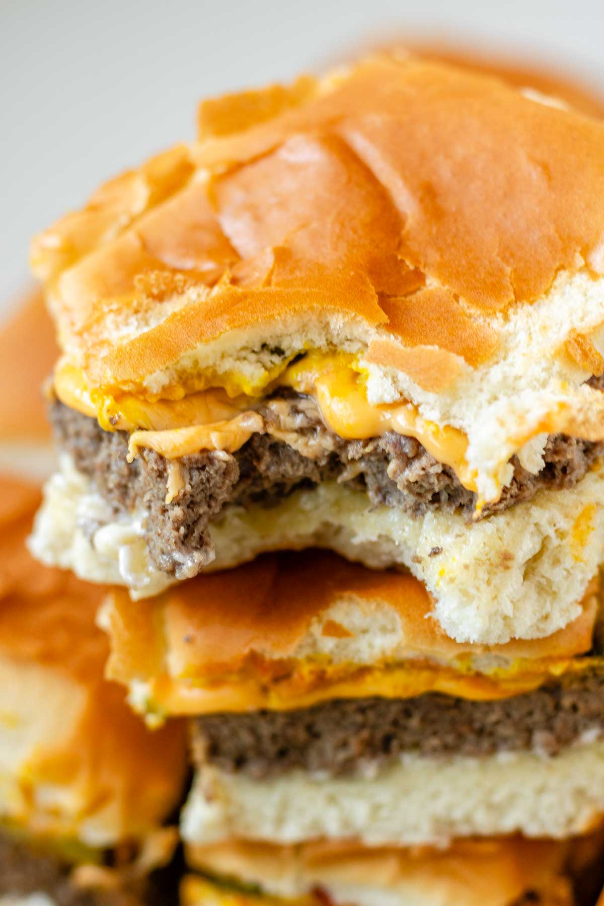 Mini burgers stacked in a pile with a bite out of one.