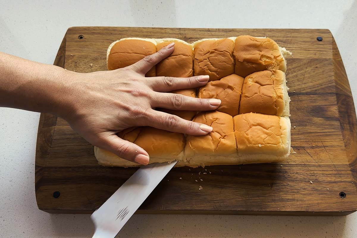A dozen buns on a cutting board are sliced in half.