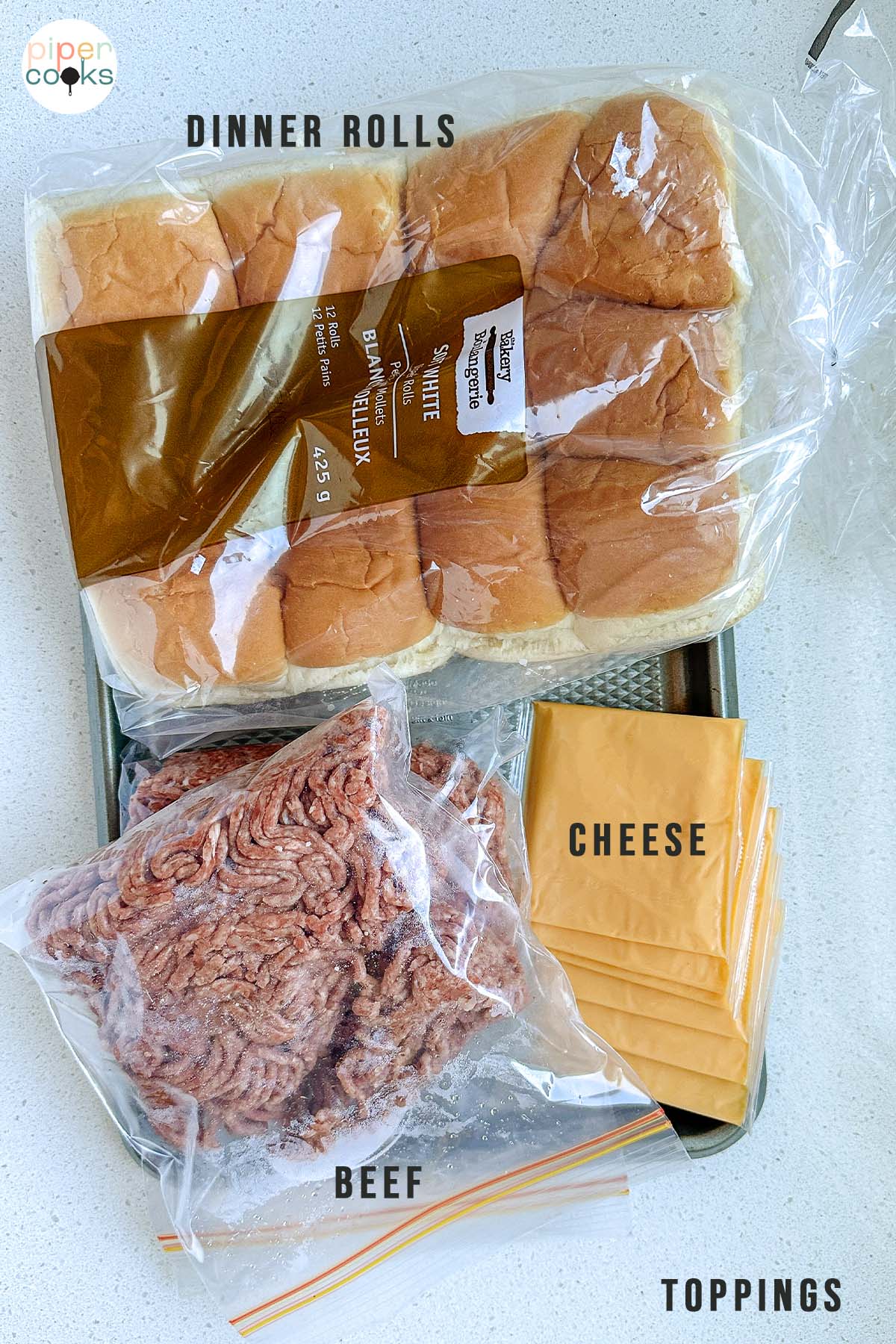 Ingredients for a recipe on a white counter labeled dinner rolls, cheese, beef, and toppings.