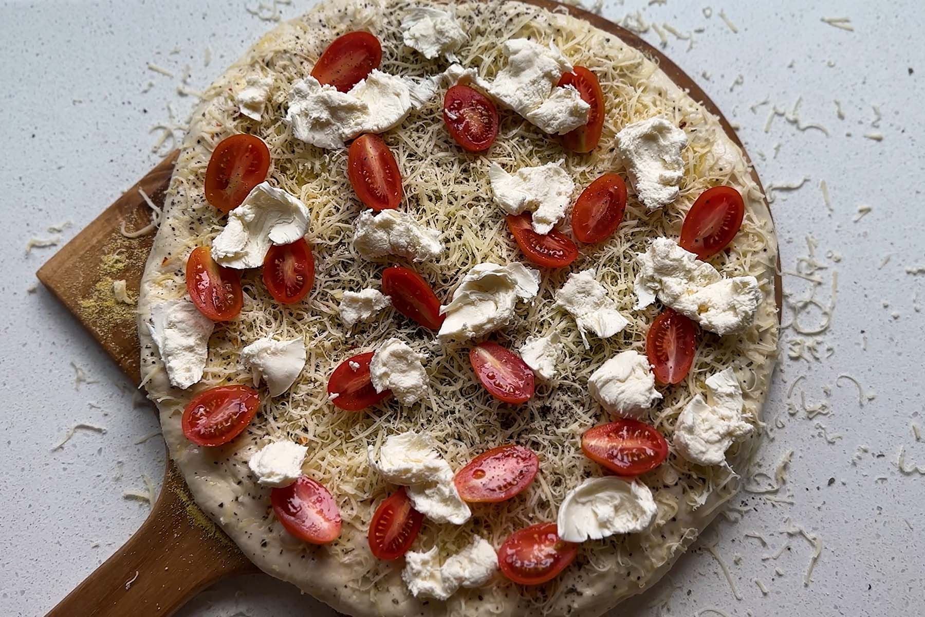 Uncooked pizza topped with cheese and halved grape tomatoes.