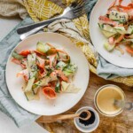 Ribbons of cucumber and carrot on a plate topped with dressing and black sesame seeds.