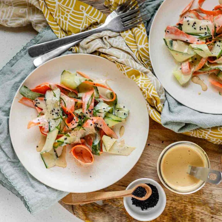 Ribbons of cucumber and carrot on a plate topped with dressing and black sesame seeds.