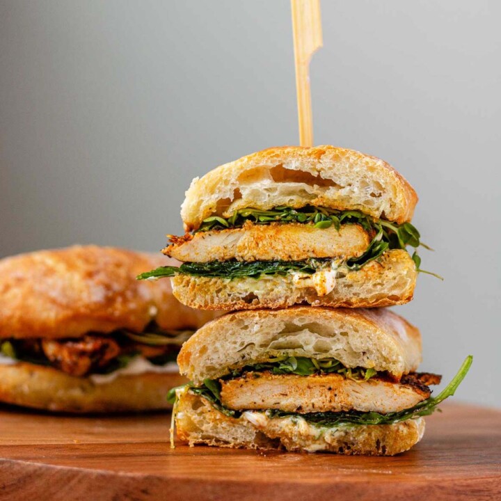 A stacked halved sandwich on a bun with chicken and spinach inside.
