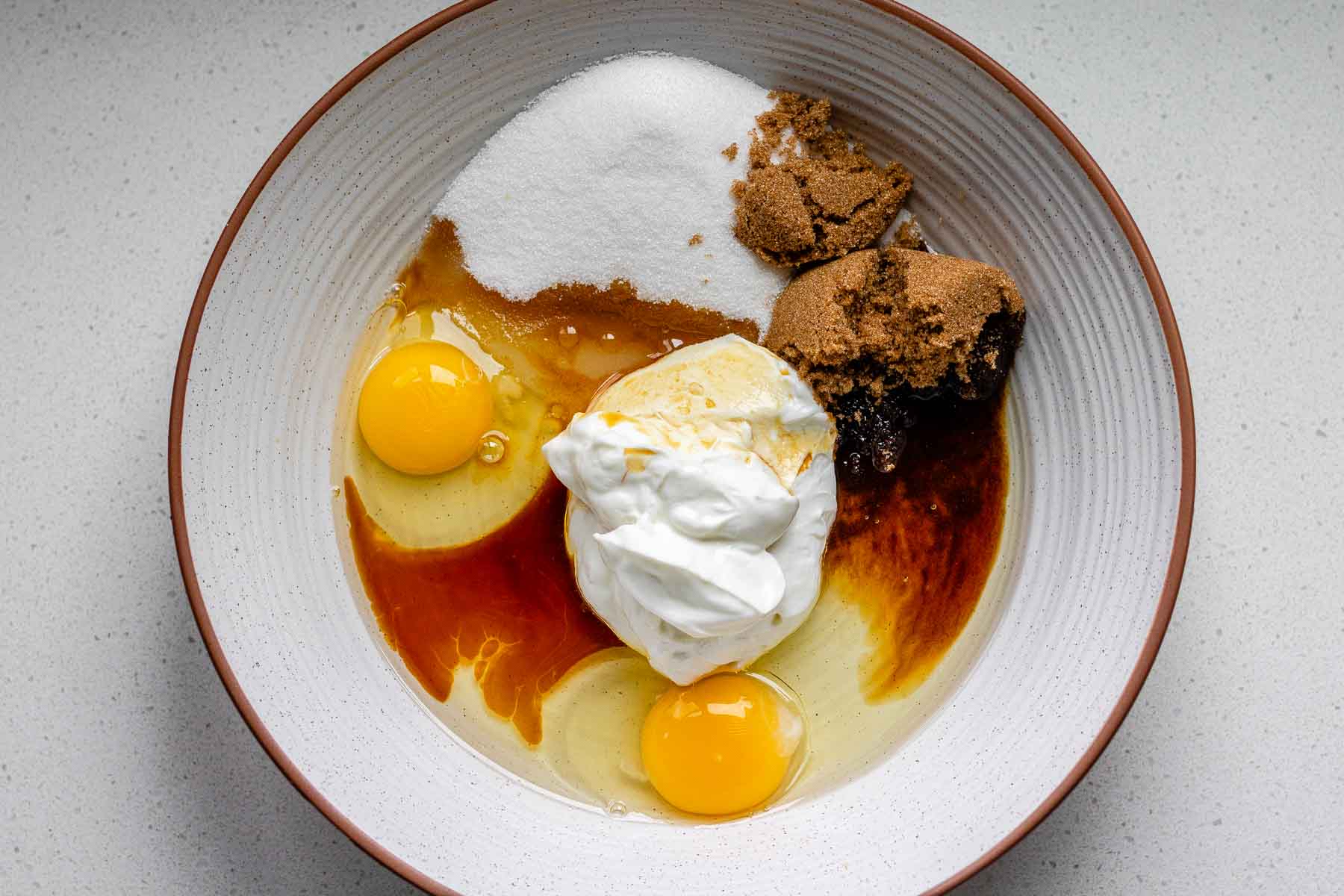 A bowl with an egg, yogurt, sugar, and brown sugar.