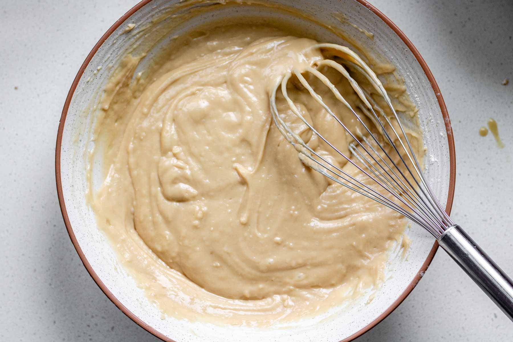 A bowl of cake batter with a whisk in it.