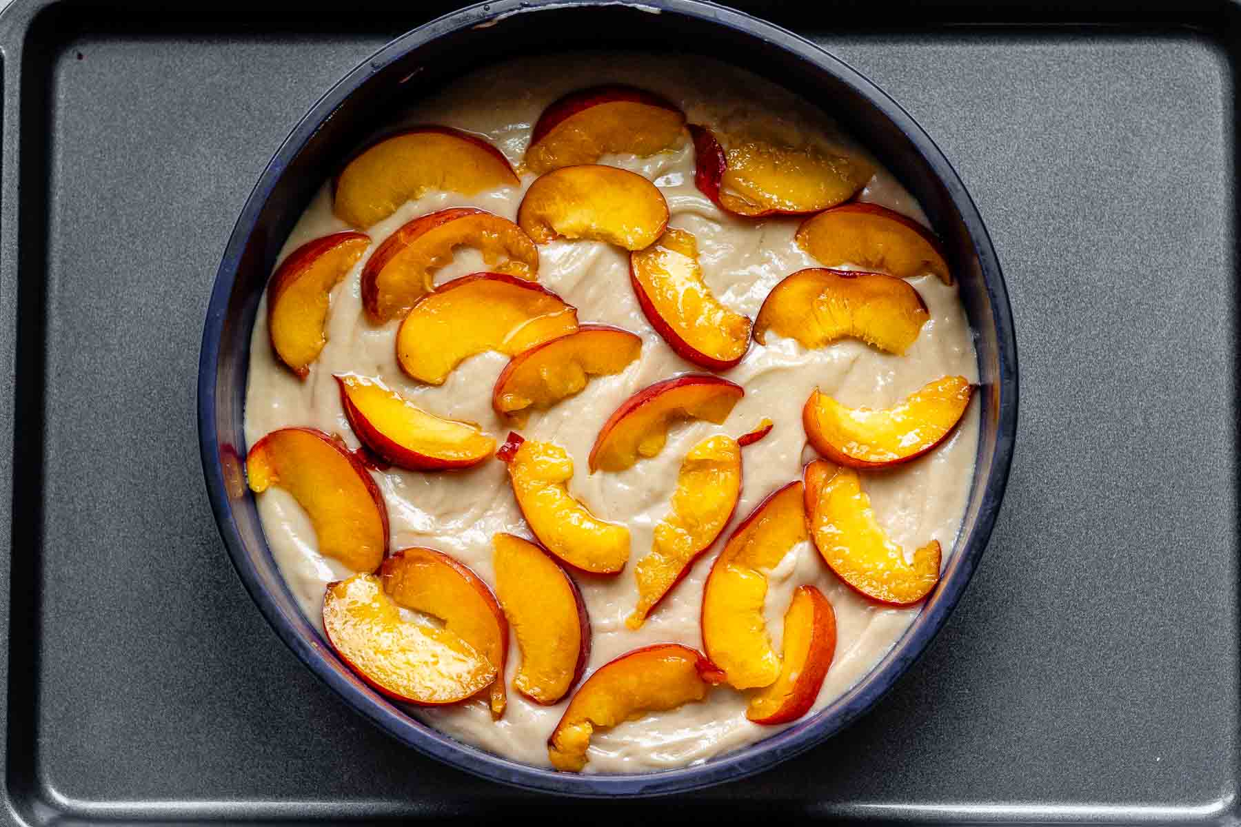 A cake pan with batter topped with peach slices.