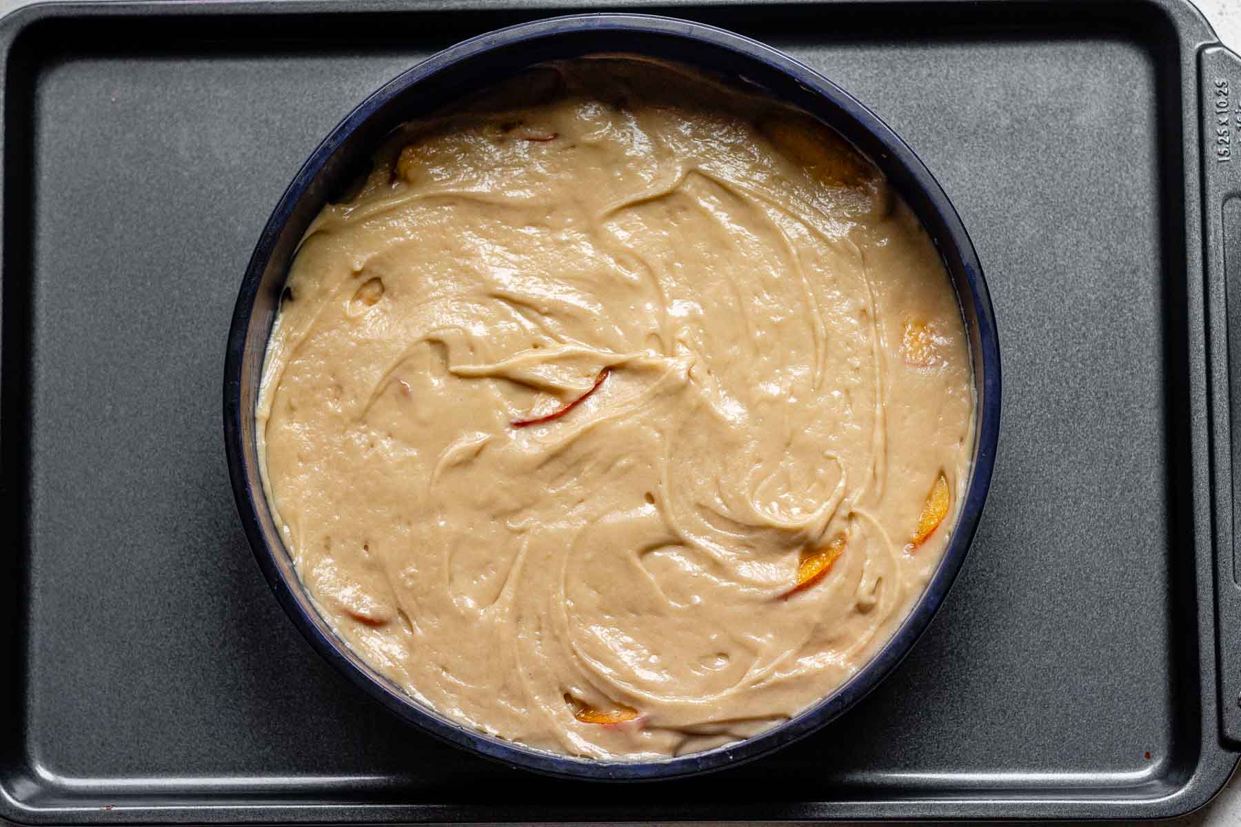 A cake pan with batter and peach slices.