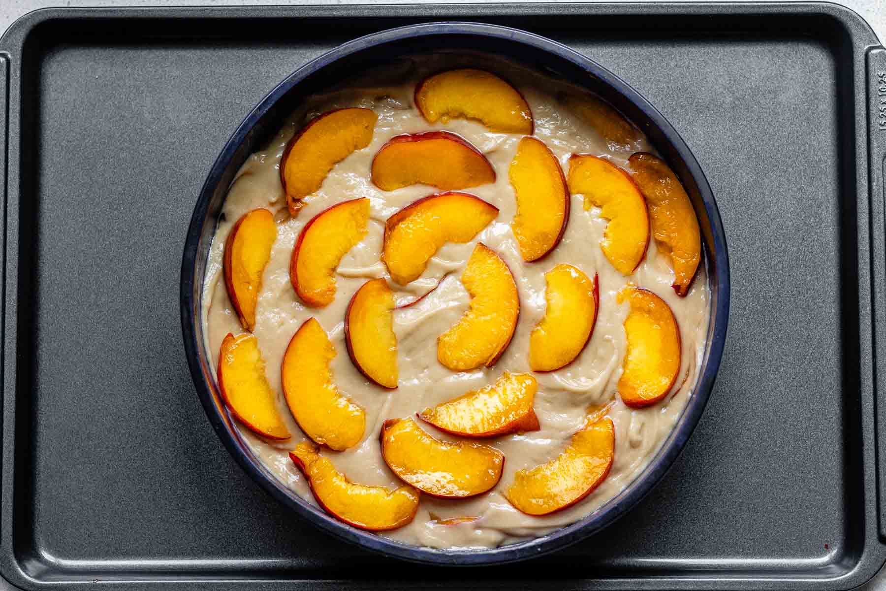 A cake pan with batter topped with peach slices.